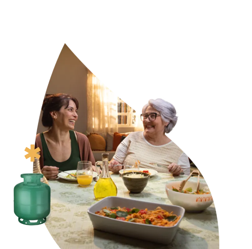 Duas mulheres sorrindo em uma mesa de jantar com pratos de comida, simbolizando momentos acolhedores proporcionados pela Copagaz.