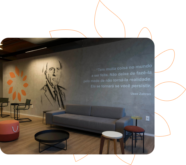 Sala de espera com sofá, mesas e uma parede decorada com o símbolo da Copa Energia, uma imagem de Ueze Zahran e uma citação