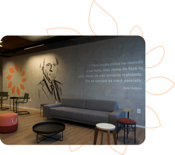 Sala de espera com sofá, mesas e uma parede decorada com o símbolo da Copa Energia, uma imagem de Ueze Zahran e uma citação